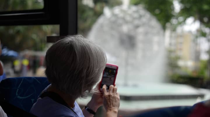 A Sydney City tour bus has stopped at Mrs Macquaries Point, a popular lookout offering stunning views of the Sydney Opera House and Sydney Harbour Bridge. Tourists are enjoying the iconic views and taking pictures.