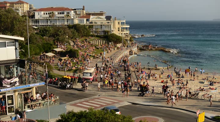 The Sydney bus tour stopped at Bondi Beach, a popular surf spot in Sydney, Australia. The beach is packed with people swimming, sunbathing, and playing volleyball. The picture is taken on the North side of Bondi Beach from Sydney Bus Tour, which is taking tourists to see the sights of the city.