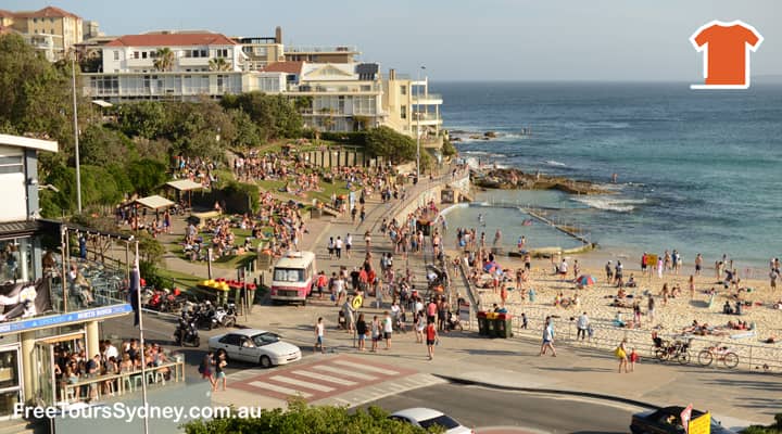 The Sydney bus tour stopped at Bondi Beach, a popular surf spot in Sydney, Australia. The beach is packed with people swimming, sunbathing, and playing volleyball. The picture is taken on the North side of Bondi Beach from Sydney Bus Tour, which is taking tourists to see the sights of the city.