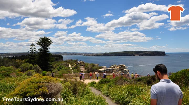 A Sydney sightseeing bus has stopped at the Gap, a popular lookout in Watsons Bay, Australia, offering stunning views of Sydney Harbour and the ocean. Tourists are enjoying the panoramic scenery and taking pictures.