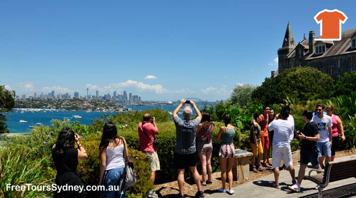 A group of tourists on a Sydney sightseeing bus tour enjoy the views of the city skyline from the lookout next to Kincoppal School in Vaucluse, Sydney, Australia. The tourists are taking pictures of the city, which is in the distance.