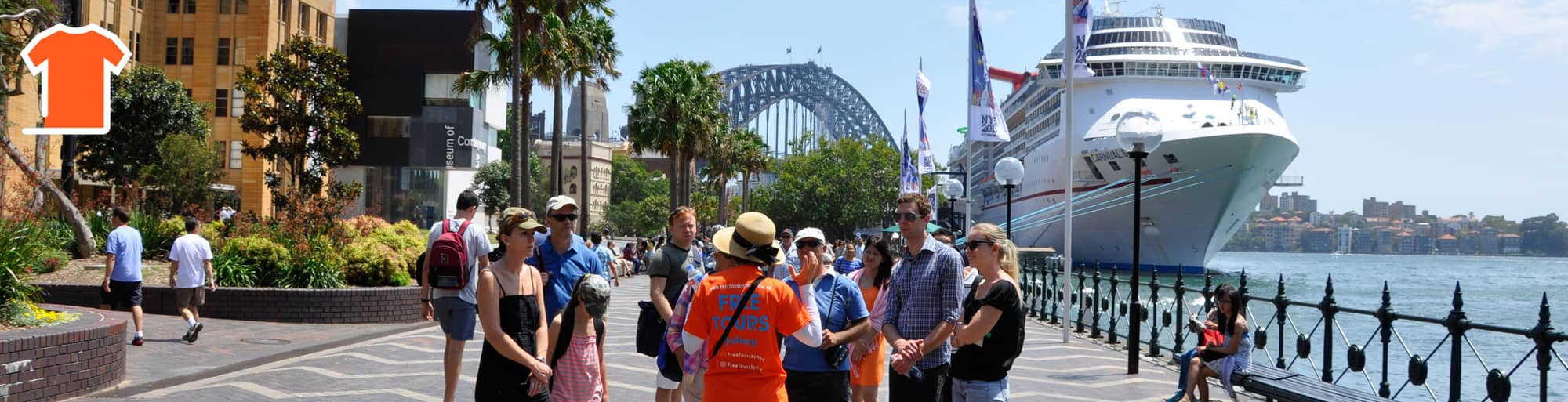 Tourists gather in Circular Quay, captivated by a tour guide in orange who shares Sydney's rich history. The iconic Sydney Harbour Bridge and a docked cruise ship complete the vibrant scene.