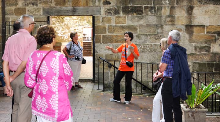 A group of travelers on a Rocks walking tour gather around the tour guide uncovering local history.