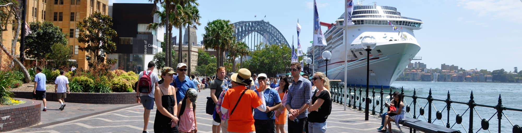 A tour guide explains the architectural details of the Sydney Opera House to a group of tourists, standing in front of the iconic landmark.