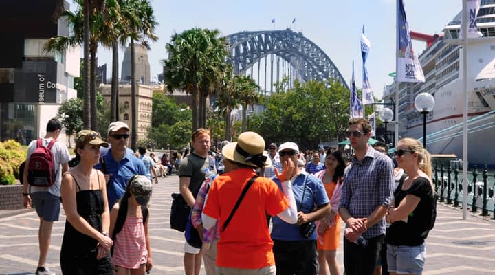 A group of travelers on a Rocks walking tour gather around the tour guide uncovering local history.